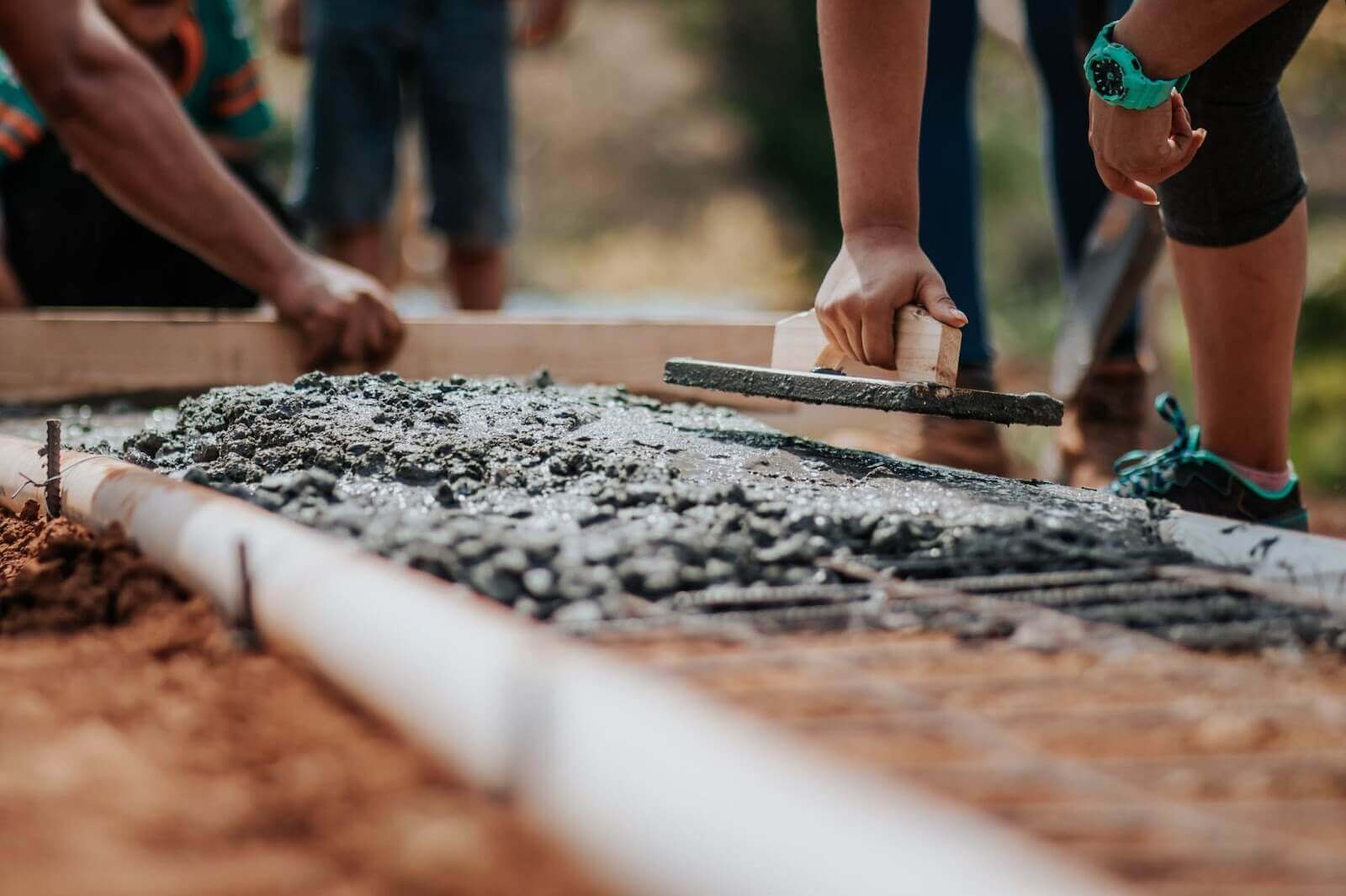 Workers spreading wet concrete over rebar frame on ground